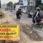 Jalan PTP Ngobo di Desa Wringin Putih, Bergas, Kabupaten Semarang rusak parah hingga membahayakan pengendara. Warga protes dengan spanduk karena sering terjadi kecelakaan akibat truk perusahaan. Senin (22/9/2025), DPU Semarang memastikan perbaikan jalan sepanjang 600 meter dengan beton segera dimulai agar aman dan tahan beban berat.