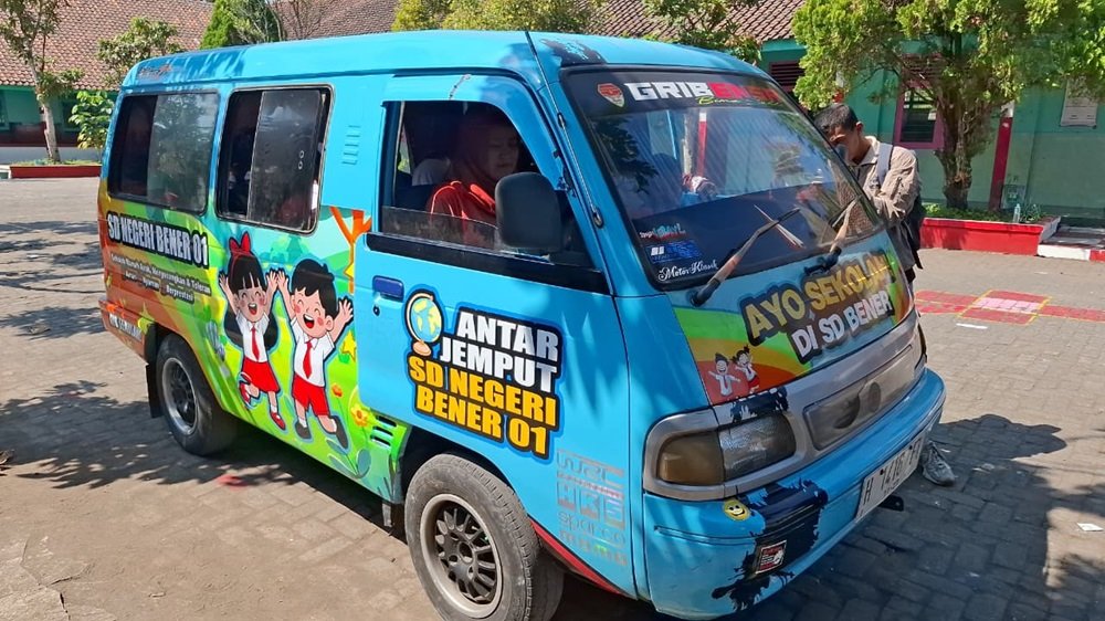 SD Negeri Bener 01 di Kecamatan Tengaran, Kabupaten Semarang, menyediakan layanan mobil antar pulang bagi siswa menggunakan bekas angkot yang dibeli dari hasil patungan guru. Program yang mulai berjalan sejak Juni 2026 ini bertujuan membantu orang tua yang kesulitan menjemput anak sekaligus meningkatkan keselamatan siswa karena lokasi sekolah berada di tepi Jalan Raya Semarang–Solo yang padat lalu lintas.